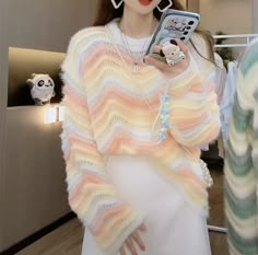 a woman holding a cell phone in her hand while wearing a colorful sweater and earrings