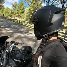 a woman wearing a helmet is sitting on her motorcycle looking at the road from behind