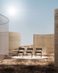 three chairs sitting in the middle of a grassy area next to two concrete silos