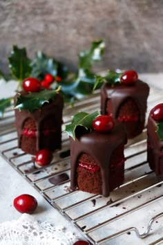 small cakes with chocolate frosting and cherries on a cooling rack next to holly