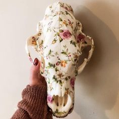 a hand holding a cow skull with flowers on it