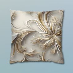 a white and gold decorative pillow on a blue background with an artistic design in the middle