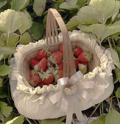 a basket filled with strawberries sitting on top of a lush green field next to leaves