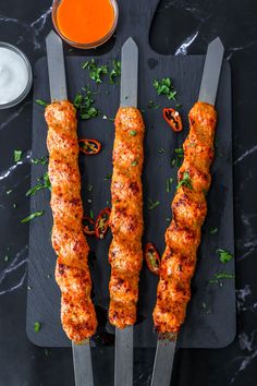 three skewers of meat with sauce and parsley on a black slate platter