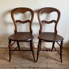 two wooden chairs sitting next to each other on top of a hard wood floored floor