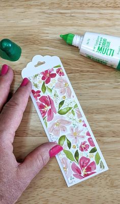 a person's hand next to some crafting supplies on a wooden table with green markers