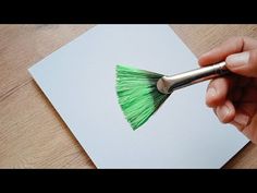 someone using a paint brush to create a green tassel on a piece of paper