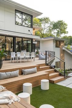 a wooden deck with white chairs and tables next to a large glass doored house