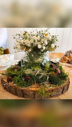 a vase filled with white flowers sitting on top of a wooden table covered in moss