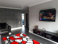 a living room with grey couches and red rugs in front of a flat screen tv