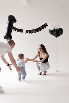 a man and woman holding hands with a baby in front of balloons that say happy birthday