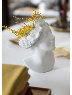 a white mannequin head with yellow flowers in it's hair sitting on a table