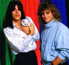 two men standing next to each other holding a white kitten