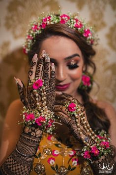 a woman wearing henna and holding her hands up to her face with flowers on it