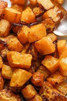 a white plate topped with cooked potatoes next to a spoon