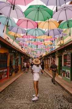 a woman walking down a cobblestone street under colorful umbrellas in the city