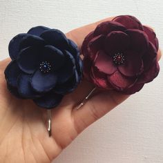 two flower hair pins in the palm of someone's hand, one is purple and one is red