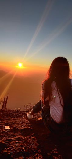 a woman sitting on top of a dirt field next to the sun in the sky