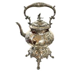 an ornate silver tea pot with a bird on it's head and handles,