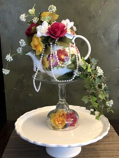 a tea pot with flowers in it sitting on a cake plate next to a wall