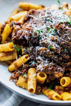 a white plate topped with pasta and meat covered in sauce, cheese and parmesan