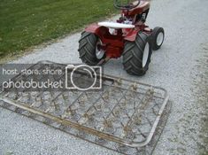 a red tractor sitting on top of a metal grate next to a grass field