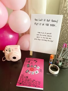 a table with balloons, a camera and a sign that says you left it out honey put it in the book