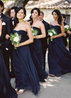 a group of people standing next to each other wearing black dresses and holding bouquets