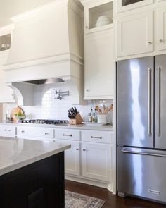 a kitchen with white cabinets and stainless steel refrigerator freezer next to an island in the middle