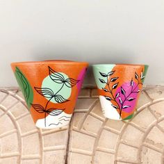 two ceramic cups sitting on top of a tile floor next to each other with leaves painted on them