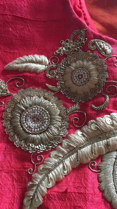 an embroidered piece with feathers and beads on a pink cloth background, close up view