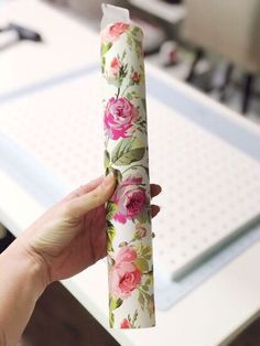 a hand holding a rolled up piece of wrapping paper with pink flowers on it in front of a computer desk