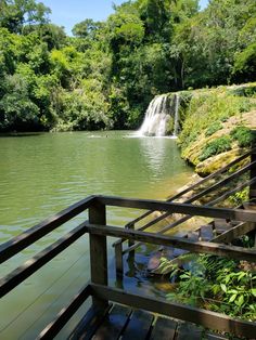 a wooden bench sitting on the side of a river next to a waterfall