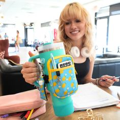 a woman sitting at a table with a blue and yellow backpack holding a water bottle