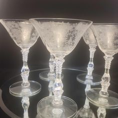 four clear wine glasses sitting on top of a glass plate, all in different shapes and sizes