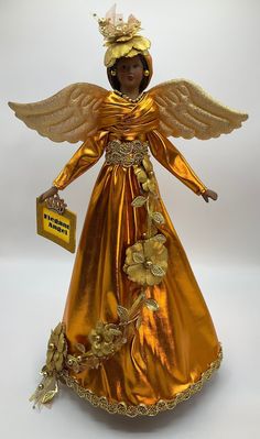 an angel figurine with gold wings and flowers on it's head, holding a tag