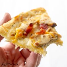 a hand holding a piece of pizza with cheese and bacon