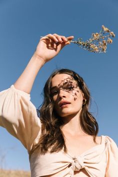 a woman with her face painted and holding a flower in front of her head, against a blue sky