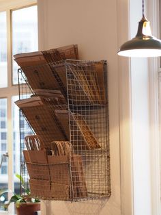 a metal basket hanging on the wall next to a window filled with boxes and utensils