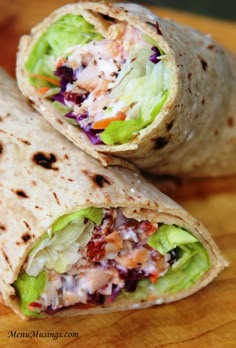 two burritos with lettuce, carrots and other toppings are on a cutting board