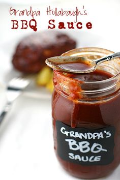 a jar of bbq sauce with a spoon in it on a plate next to other food