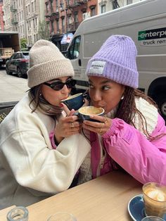 two women sitting at a table with food in front of them and one holding a cup