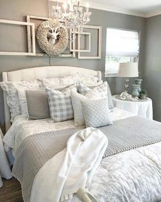 a white bed topped with lots of pillows next to a chandelier and window