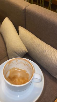 a cup of coffee sitting on top of a white saucer next to a brown couch