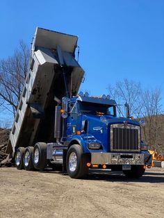 a dump truck with its load in the back is parked on a dirt road next to some trees