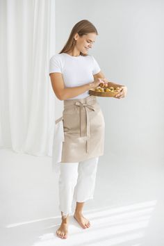 a woman in white shirt and tan apron holding a plate with food on top of it