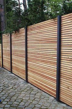 a wooden fence that is next to a brick walkway with black posts on the sides