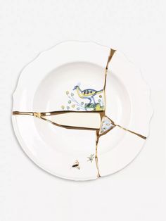 a broken white plate with two birds on it's side and gold trimming around the edge