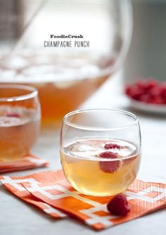 two glasses of champagne punch with raspberries in the background