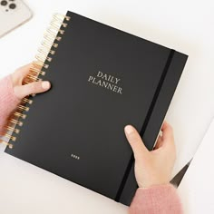 a person is holding a daily planner in their hand and pointing to it on the desk